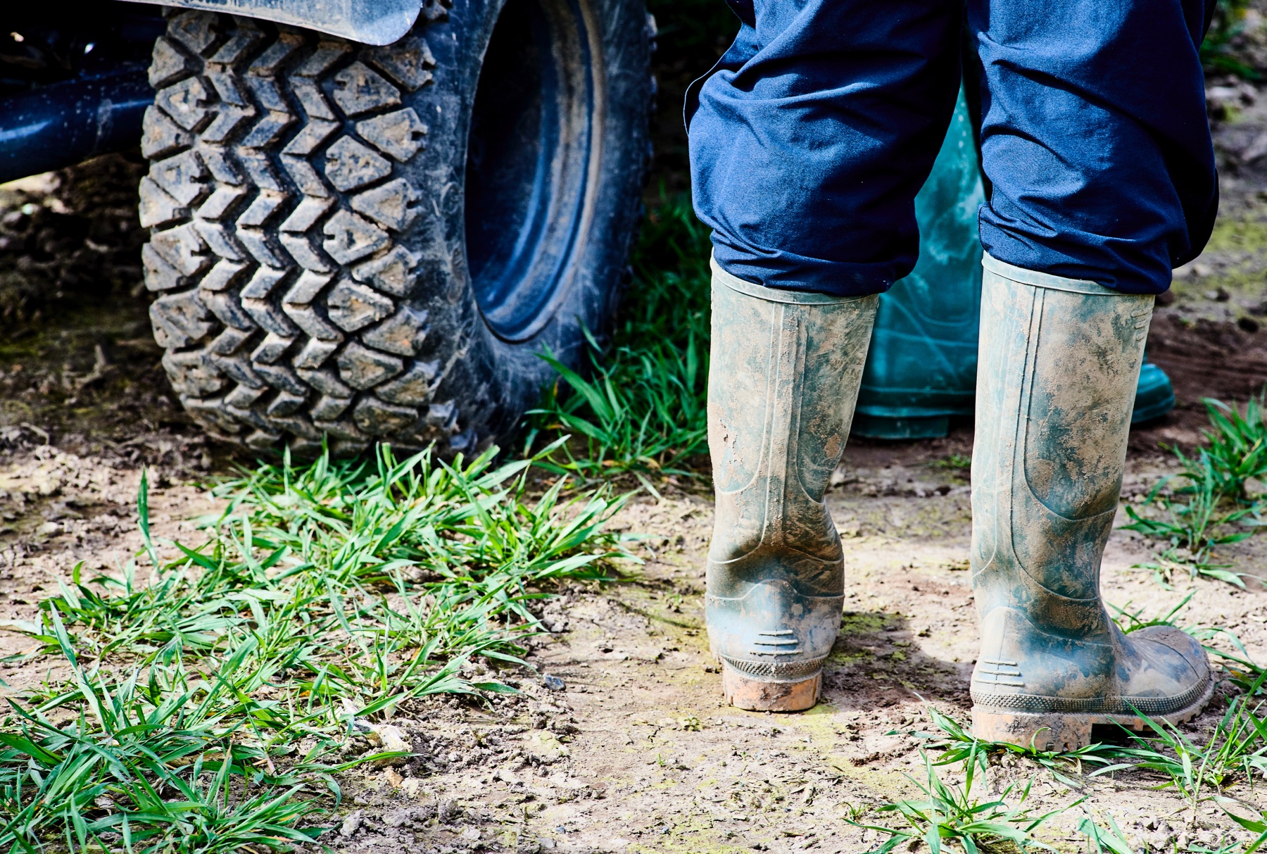 A Farm worker wearing muddy Welly Boots next to a farm vehicle